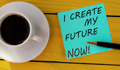 I CREATE MY FUTURE NOW! - words on a green sheet on a yellow wooden background with a pen and a cup of coffee