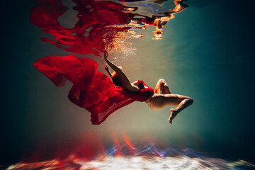 Art work. A slender, tanned girl with an athletic figure and blond hair, with red material and light underwear, in a ballet pose underwater in the pool. Aesthetic image for your design or decoration.
