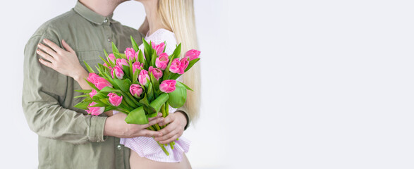 Young couple hugging with bouquet of tulips in hand isolated on white background. Space for text on the right