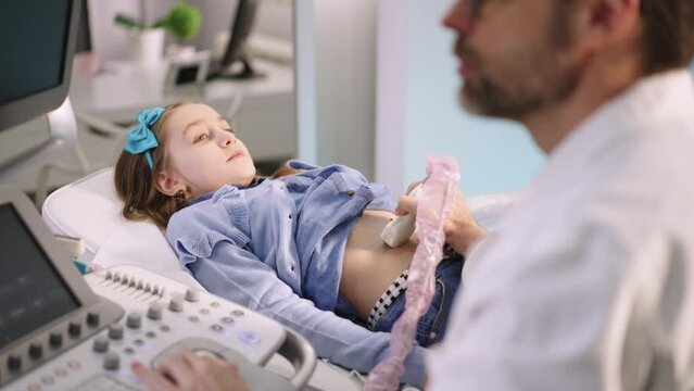 Cute little girl having ultrasound procedure of internal organs with sonographer at medical clinic. Pediatric abdominal ultrasound