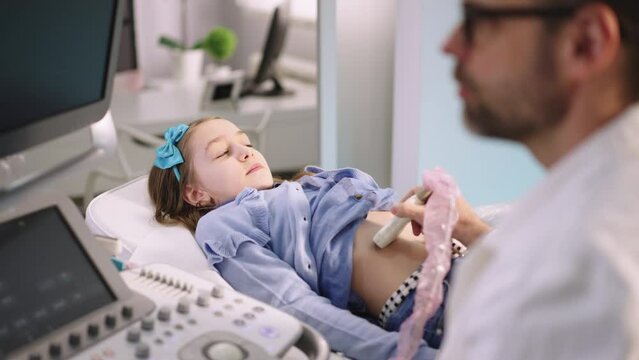 Close-up of a little girl patient receives belly diagnostics with ultrasound machine from a professional