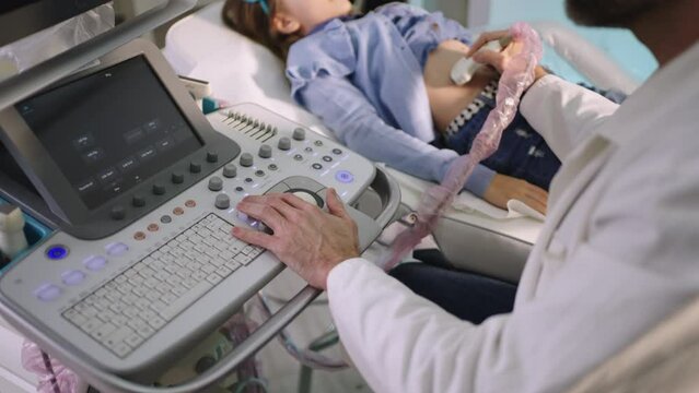 Professional male doctor taking sonogram of little patient girl's belly with digital equipment the medical clinic
