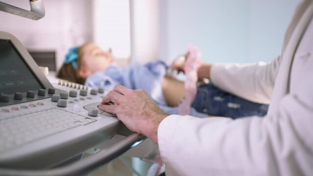 Little cute girl getting ultrasound scan from doctor. Professional confident male doctor, checking girl's internal organs of belly with ultrasound transducer scanner