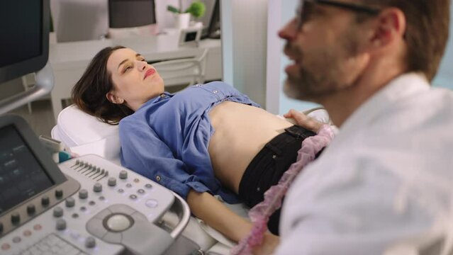 Portrait of a beautiful young woman having ultrasound scanning of her belly. Ultrasound procedure of internal organs with sonographer