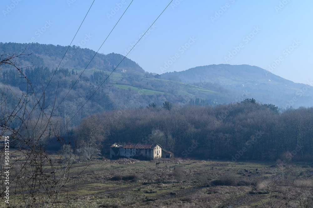 Wall mural landscape of an old ruined farmhouse in the Basque country, on a misty winter morning in the plain, in the background the green hills, above the blue sky,