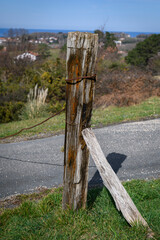 close-up of an old wooden post marked by the passage of time from which a rusty iron cable hangs,...