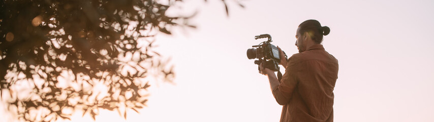 A young Caucasian man with a professional camera in his hands on a mountain by the sea.