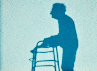 Shadow, disability and walking with a senior woman outdoor on a blue wall background on a sunny...