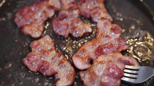 A chef fries some slices of bacon and turns them regularly until they are cooked through and really crispy.