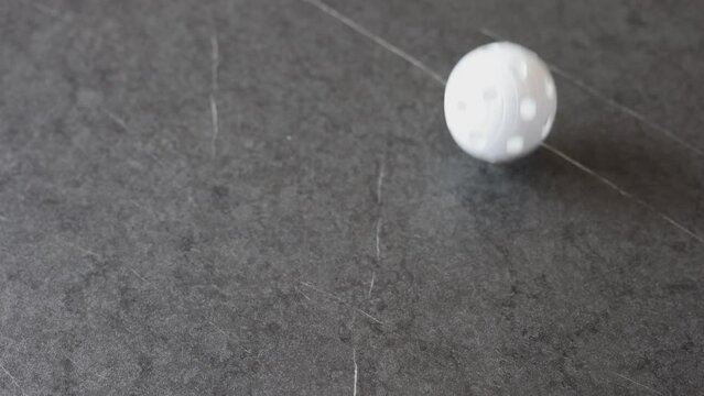 A floorball ball rolls and bounces over a black table.