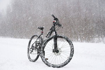 Fototapeta na wymiar A black bicycle on a snowy road in the forest during a heavy snowfall in winter