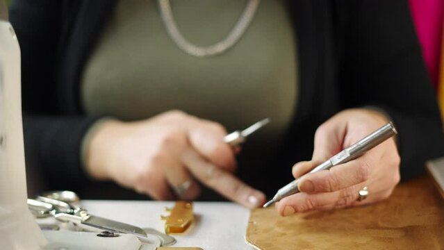 Leather worker's hands making holes in a small piece of leather with a hammer and perforator in slow-motion at workshop