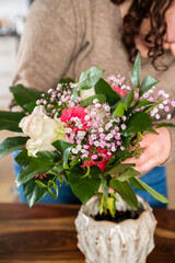 Female florist with brown curly hair holding a bunch of colorful spring flowers, vertical shot, indoors on a wooden table