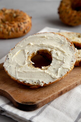 Homemade Whole Grain Bagel with Cream Cheese on a rustic wooden board, side view. Close-up.
