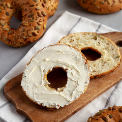 Homemade Whole Grain Bagel with Cream Cheese on a rustic wooden board, side view.