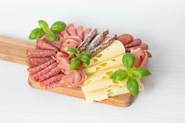 Cheese, sausage, salami on a wooden square board.