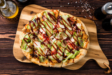 Italian food pizza with chicken, bacon, cucumbers, tomatoes and barbecue sauce on a thick dough.