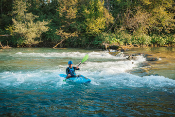 Young teenager cruising down whitewater rapids in a blue kayak, beautiful river nature on a sunny summer day, handheld shot.