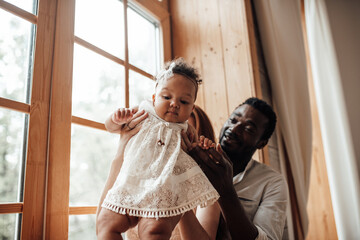Portrait of candid friendly happy interracial family with swarthy baby together near window