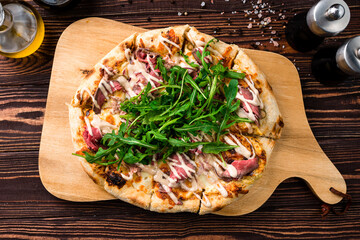 Italian pizza with beef, bacon, cheese, arugula and sauce on a thick dough.