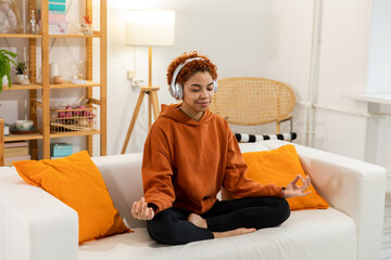 Yoga mindfulness meditation. Young healthy african girl practicing yoga at home. Woman sitting in lotus pose on yoga mat meditating smiling relaxing indoor. Girl doing breathing practice, yoga at home