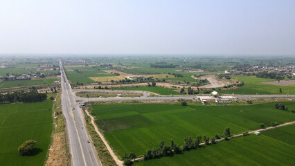 Fototapeta na wymiar An aerial view of Lahore-Sialkot Motorway's Muridkay interchange, capturing vehicles moving on the highway in the vicinity of green rice fields. 