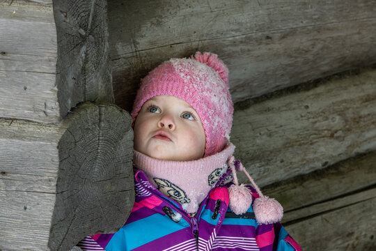 A little girl enjoys the sunny and cold winter wonderland of the north. The old log walls crackle from the frost.