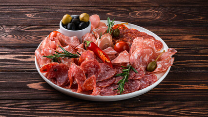 Meat plate with slices of sausage, ham, olives, cherry tomatoes and rosemary.