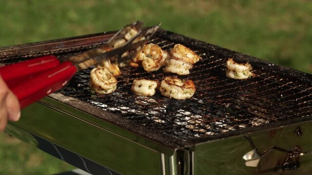 Cooked shrimps pick up from BBQ grill. Grilled fresh shrimps, barbeque sea food on fire flaming hit from real wood logs. Summer camping cooking in the park and leisure.