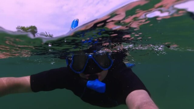 Close up split view of selfie of a man snorkelling in mask, dive underwater in lake. Freediver in sport dress glides underwater and above water in transparent clean water. Freedive and self-portrait