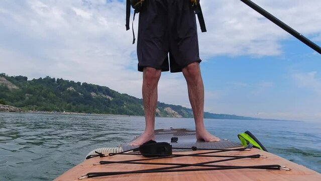 Man standing on SUP and paddling. Stand up paddling surfboard fitness sport. Popular tourist water sport exercising workout on Inflatable stand up paddleboarding, rowing. Recreation and wellness.
