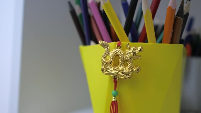 Closeup of little keychain with golden chinese dragon with colourful pencils in classroom. Learning Chinese language concept. 