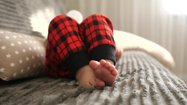 Close up shot of child feet. Little newborn baby boy lies on a bed at home. Lonely kid in plaid pajamas peacefully rests in a cozy bed. New life, parenthood concept. Selective focus