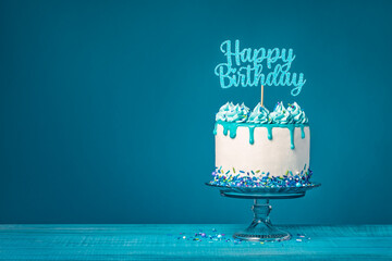White happy birthday drip cake with teal ganache over blue background - 580157582