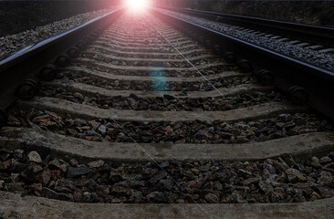 railway rails from a low shooting point go into a distant perspective, from which a bright light is...