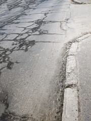 wet cracks on the asphalt surface of the road, a broken curb