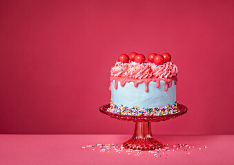 Birthday Drip Cake on a red stand and colorful sprinkles on a vibrant pink background - 580157970