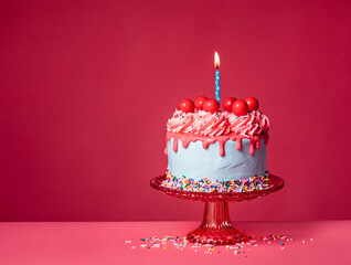 Birthday Drip Cake with lit candle on a red stand with colorful sprinkles on a vibrant pink background - 580158165