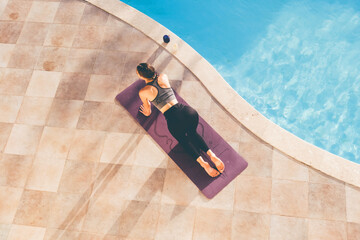 Young woman practicing yoga at the poolside in the evening.