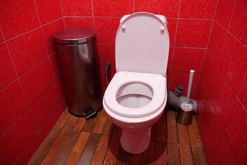 Toilet room with toilet bowl, wastebasket, toilet brush and red wall tiles