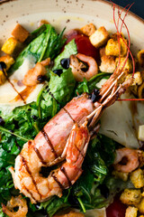 Italian cuisine Caesar salad with crawfish, shrimp, parmesan cheese, lettuce, tomatoes, croutons on a dark table.