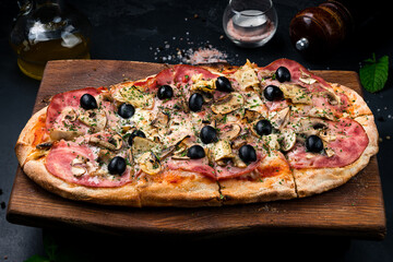 Italian food pizza with ham, mushrooms, cheese, olives and greens on a wooden board.