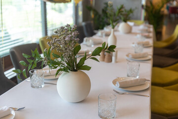 Dried flowers in a round white vase as table decoration for a wedding party. Cutlery and glasses.