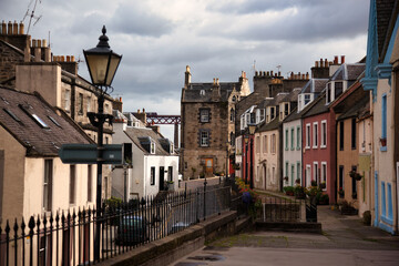 Queensferry High Street, Scotland with colorful Tenement Houses. Firth of Forth Bridge in background 1890.