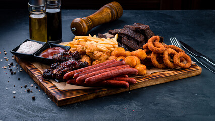Set of snacks fried croutons, french fries, sausages, squid rings, chicken nuggets, cheese balls and sauces.