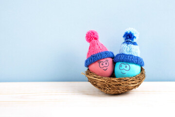 Fototapeta na wymiar Two Easter eggs with funny faces and crocheted hats in a decorative nest of sisal on a wooden table. Happy Easter concept. Greeting card.
