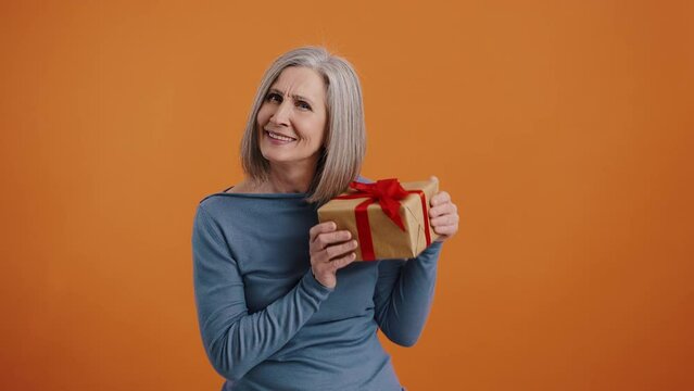 Senior woman holds gift box with red ribbon smiling cutely