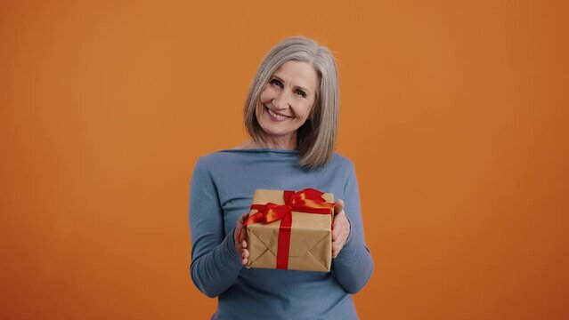 Smiling senior woman presents gift in box with red bow
