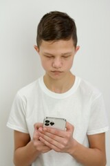 boy of 10-15 years old is standing on white background with phone in hands he is playing games or browsing social network
