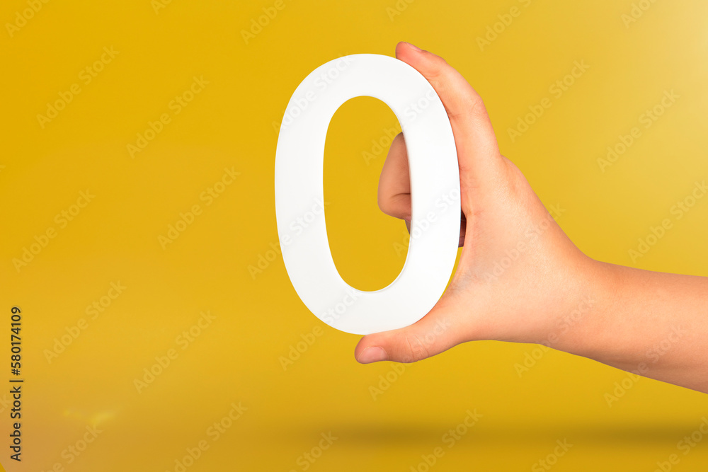 Leinwandbilder numeral zero in hand. a hand holds a white number zero on a yellow background with copy space. zero 